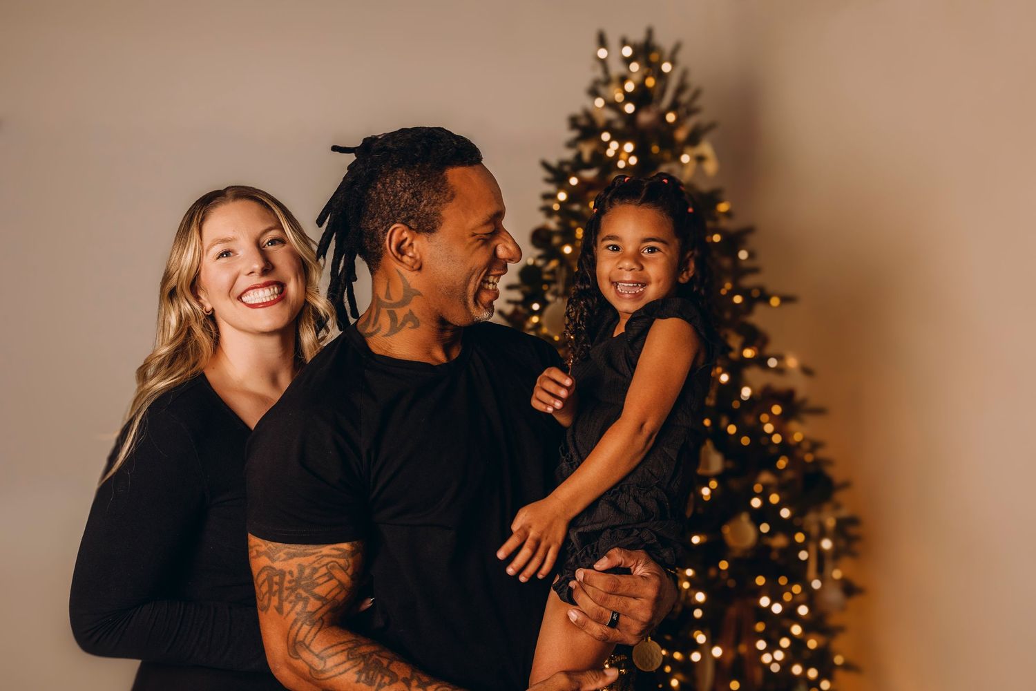 Family of four smiling together in front of a decorated Christmas tree, dressed in festive holiday attire.