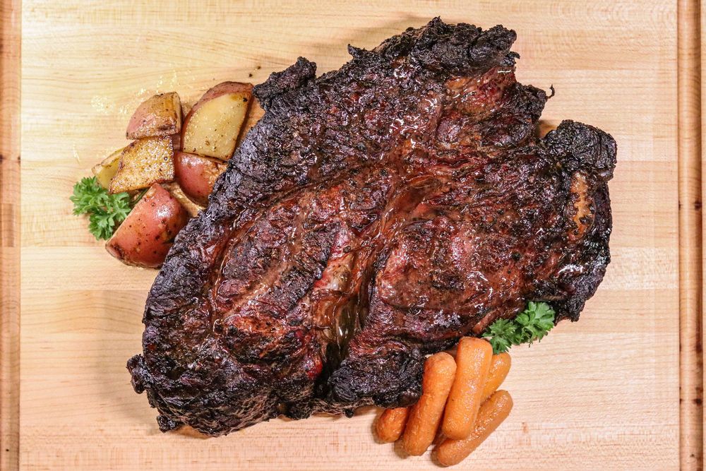 Juicy BBQ beef brisket on a wooden cutting board with roasted red potatoes, carrots, and fresh herbs.