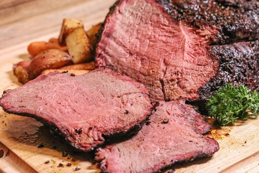 Sliced smoked beef brisket on a wooden cutting board with roasted potatoes and fresh herb garnish.