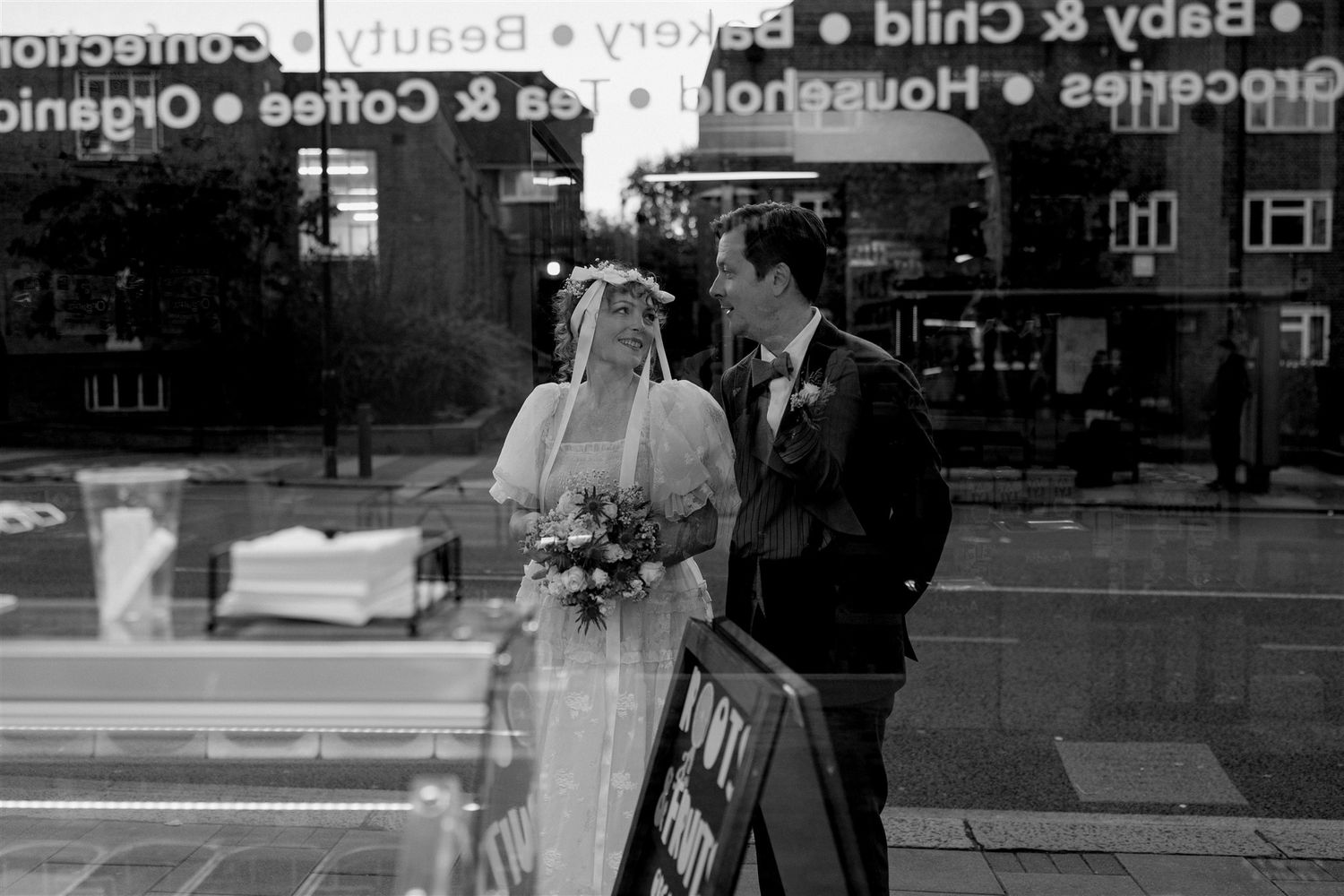 Black and white photo of a bride and groom sharing a moment outside a shop on their wedding day.