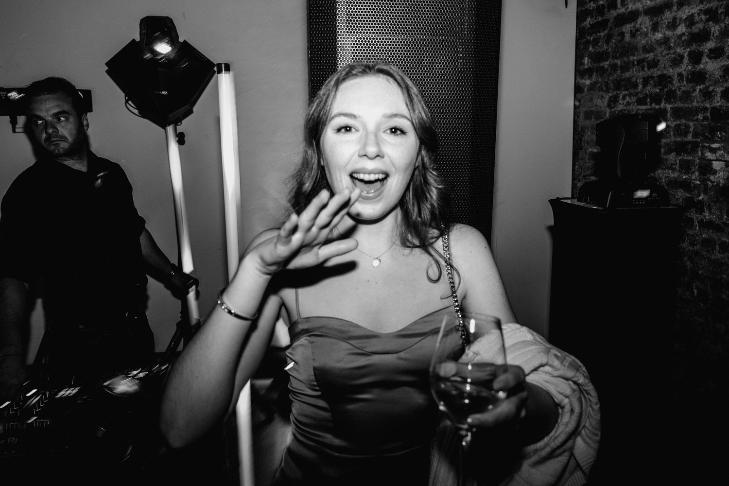 Black and white photo of a young woman laughing and holding a drink at a party event.