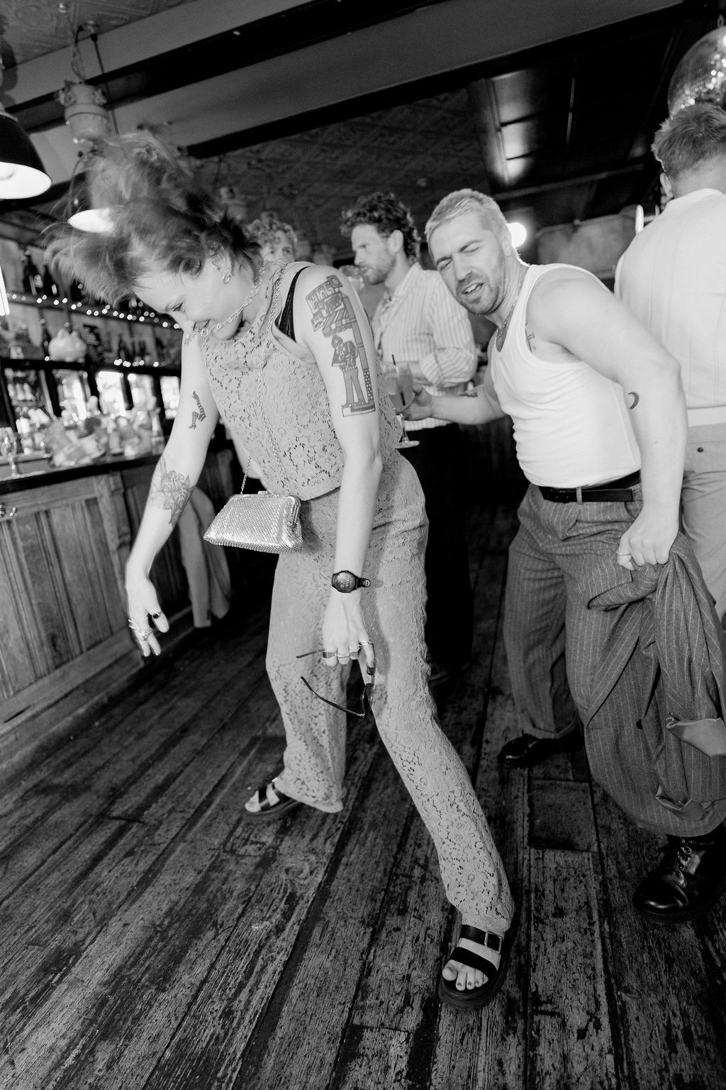 Black and white photo of guests dancing energetically at a wedding reception in a rustic bar venue.