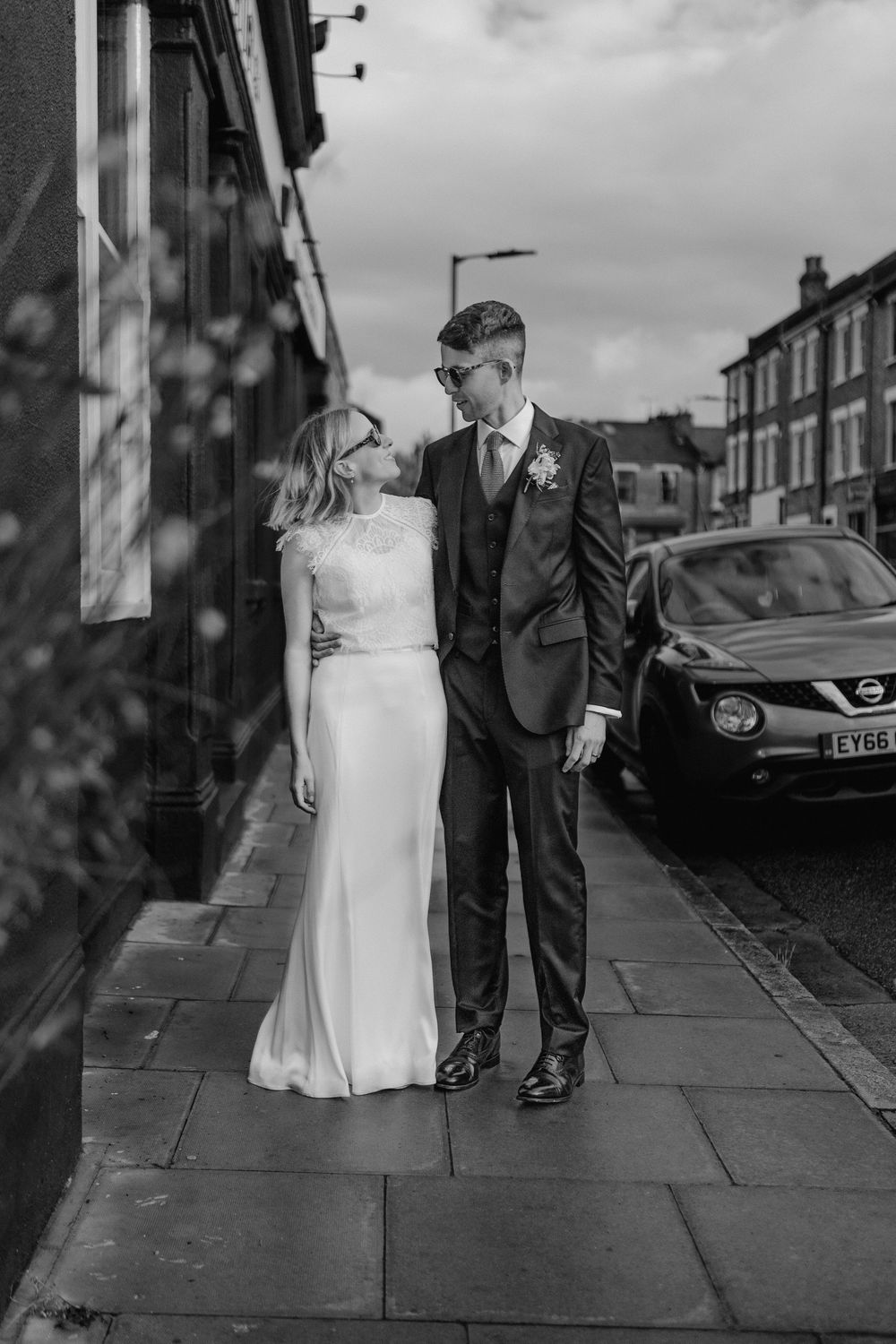 Black and white photo of a bride and groom standing on a sidewalk, gazing at each other on their wedding day.