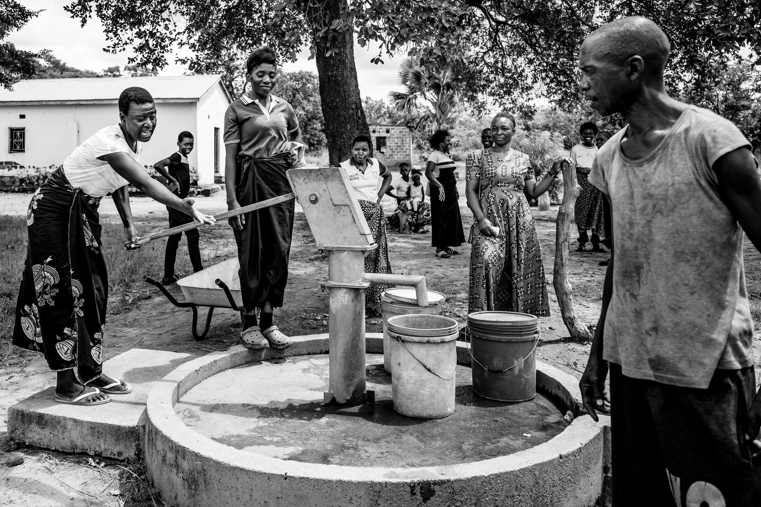 Black and white photo of African villagers pumping water from a communal well outdoors.