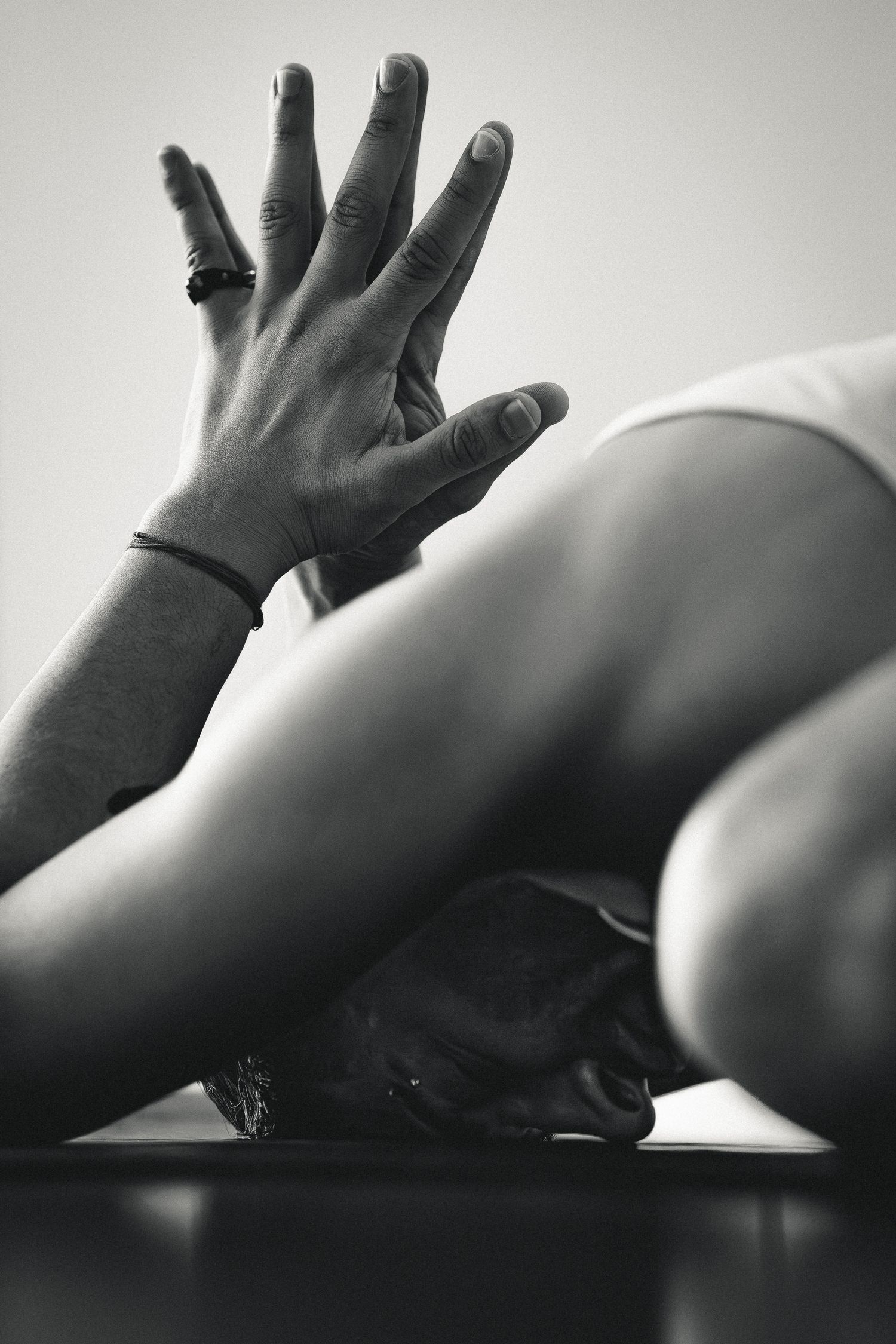 Close-up of a hand with rings pressing against legs during a seated yoga forward fold pose, black and white photo.