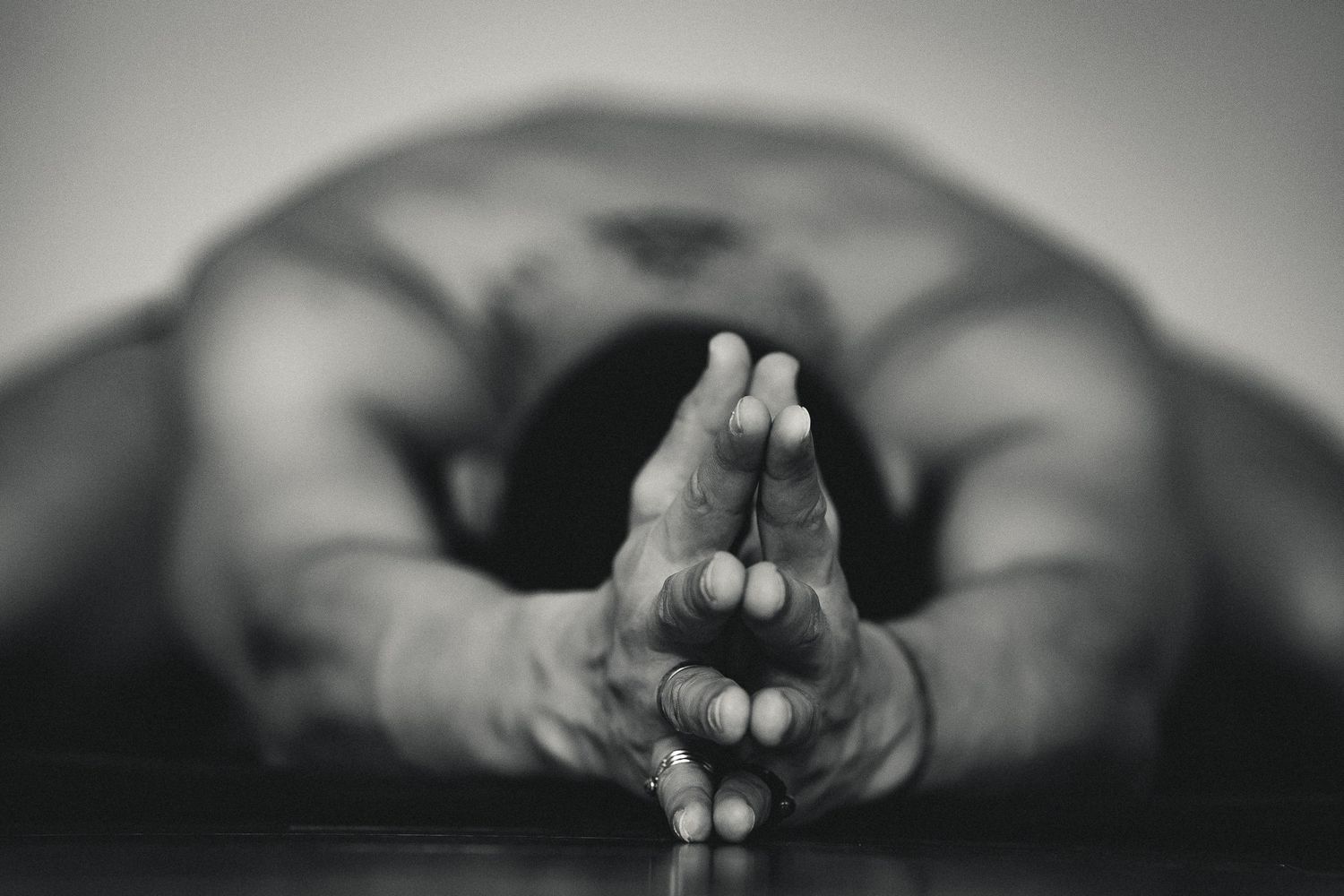 Black and white close-up of hands pressed together in prayer pose during yoga practice.