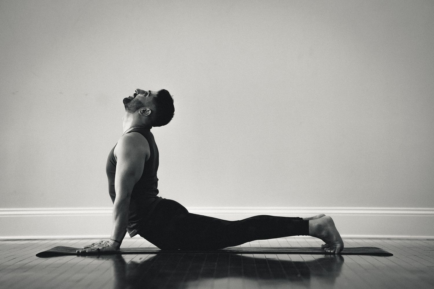 Black and white photo of yogi in cobra pose stretch on wooden floor.