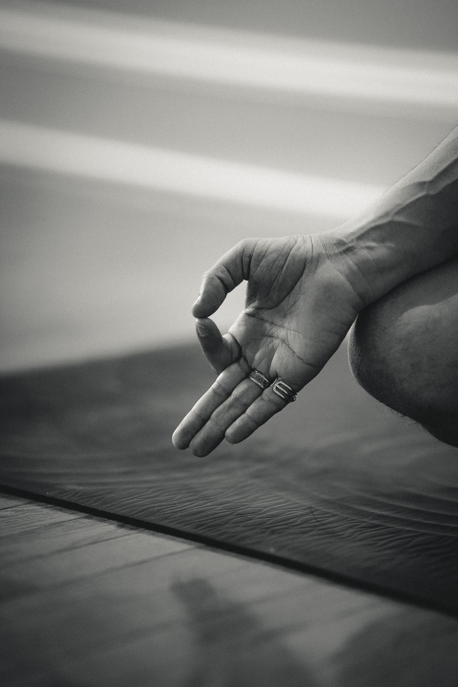 Close-up of a hand in gyan mudra meditation gesture with rings on fingers resting on a yoga mat, black and white.