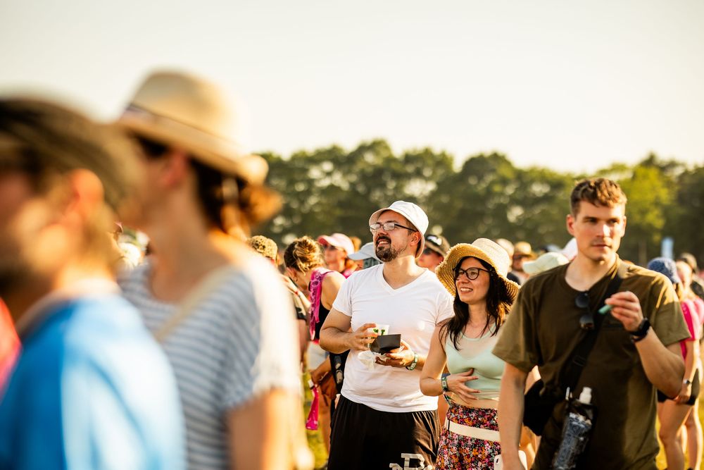 Festival goers enjoying a sunny day walking through a crowded outdoor summer music festival.