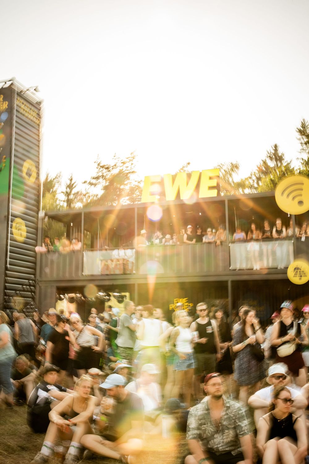 Blurred motion shot of festival crowd in front of the glowing EWE sponsor stage at golden hour.