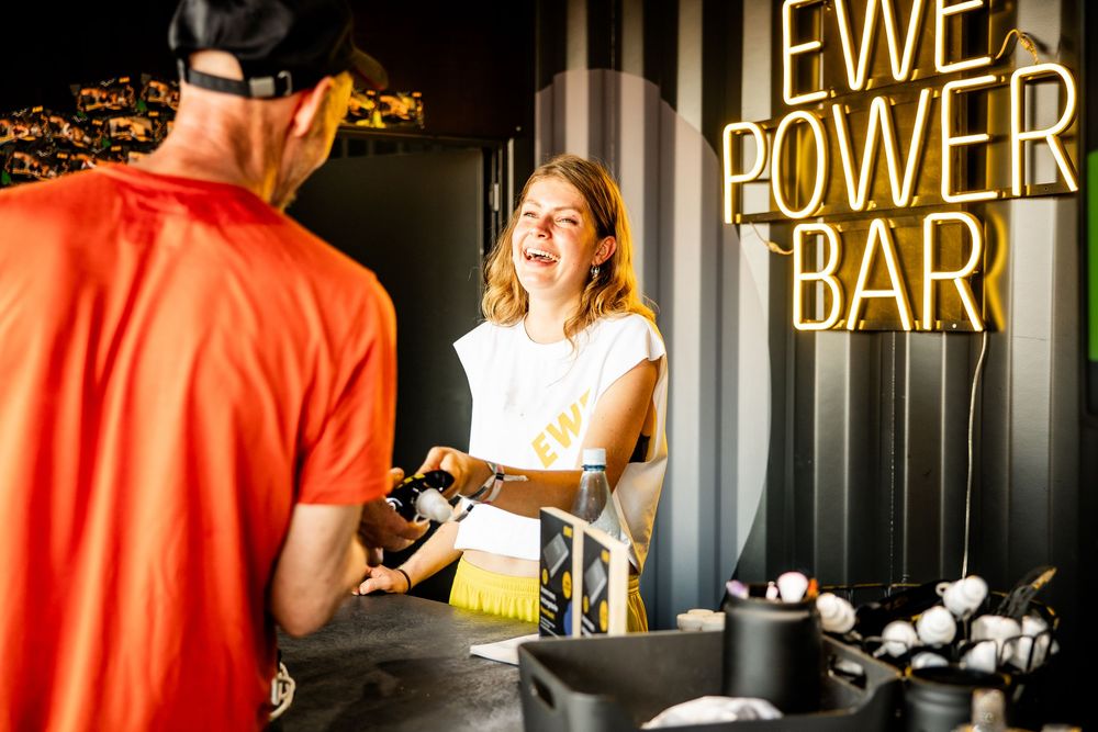 Smiling female bartender serving customer at EWE Power Bar with striped black and white walls.