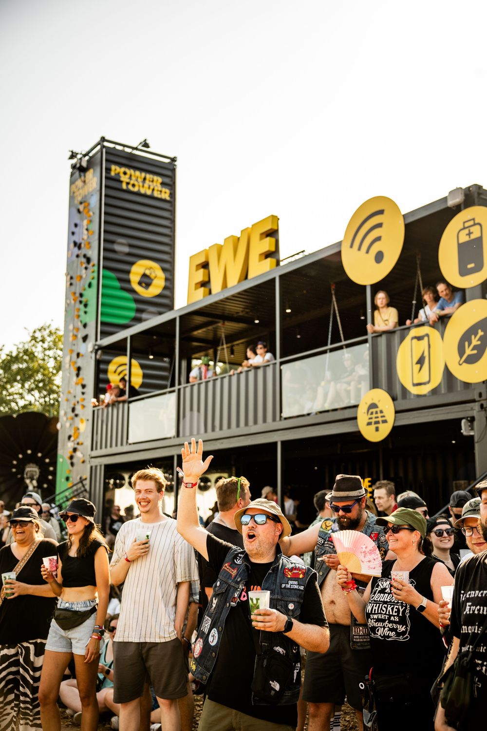 Crowd of festival-goers in front of EWE Power Tower at an outdoor music festival on a sunny day.