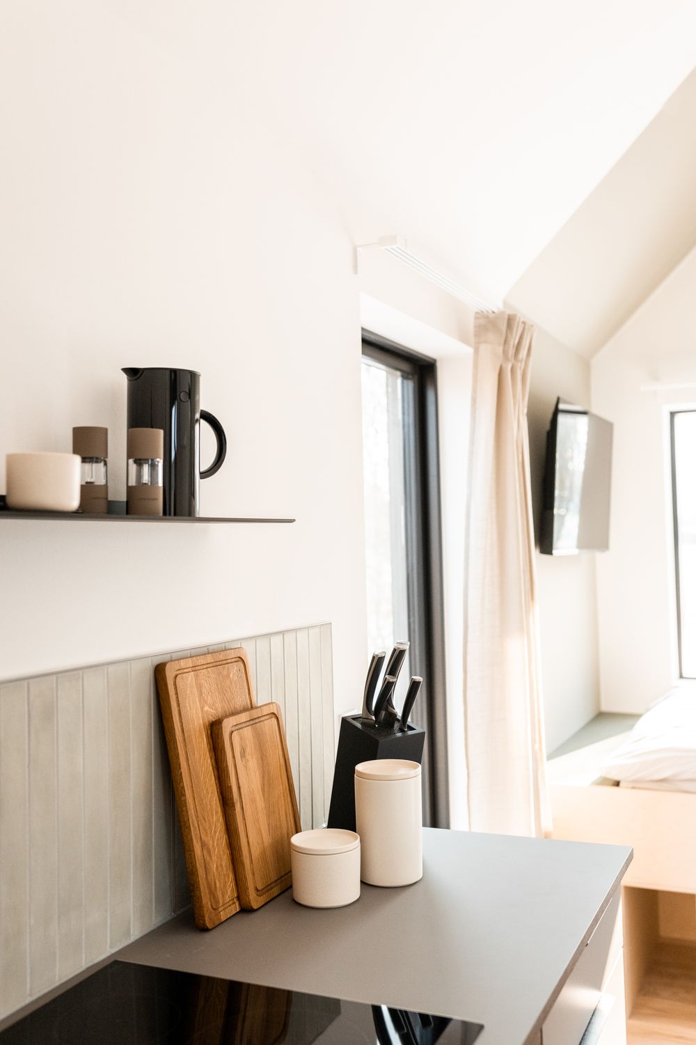 Compact cabin kitchen with induction cooktop, wooden cutting boards, knife block, and open shelving.