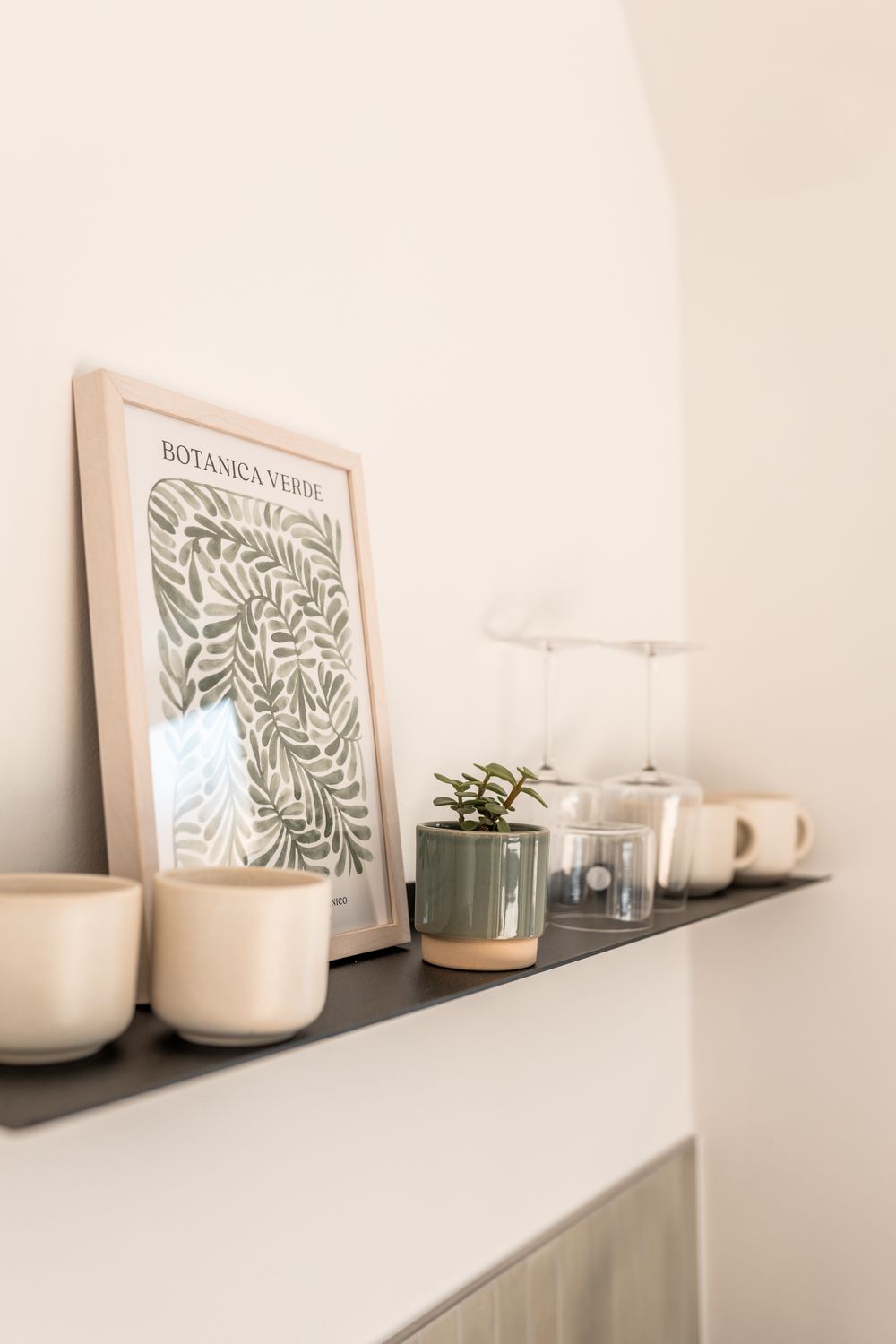 Minimalist shelf display with Botanica Verde framed print, ceramic cups, small succulent, and glassware.
