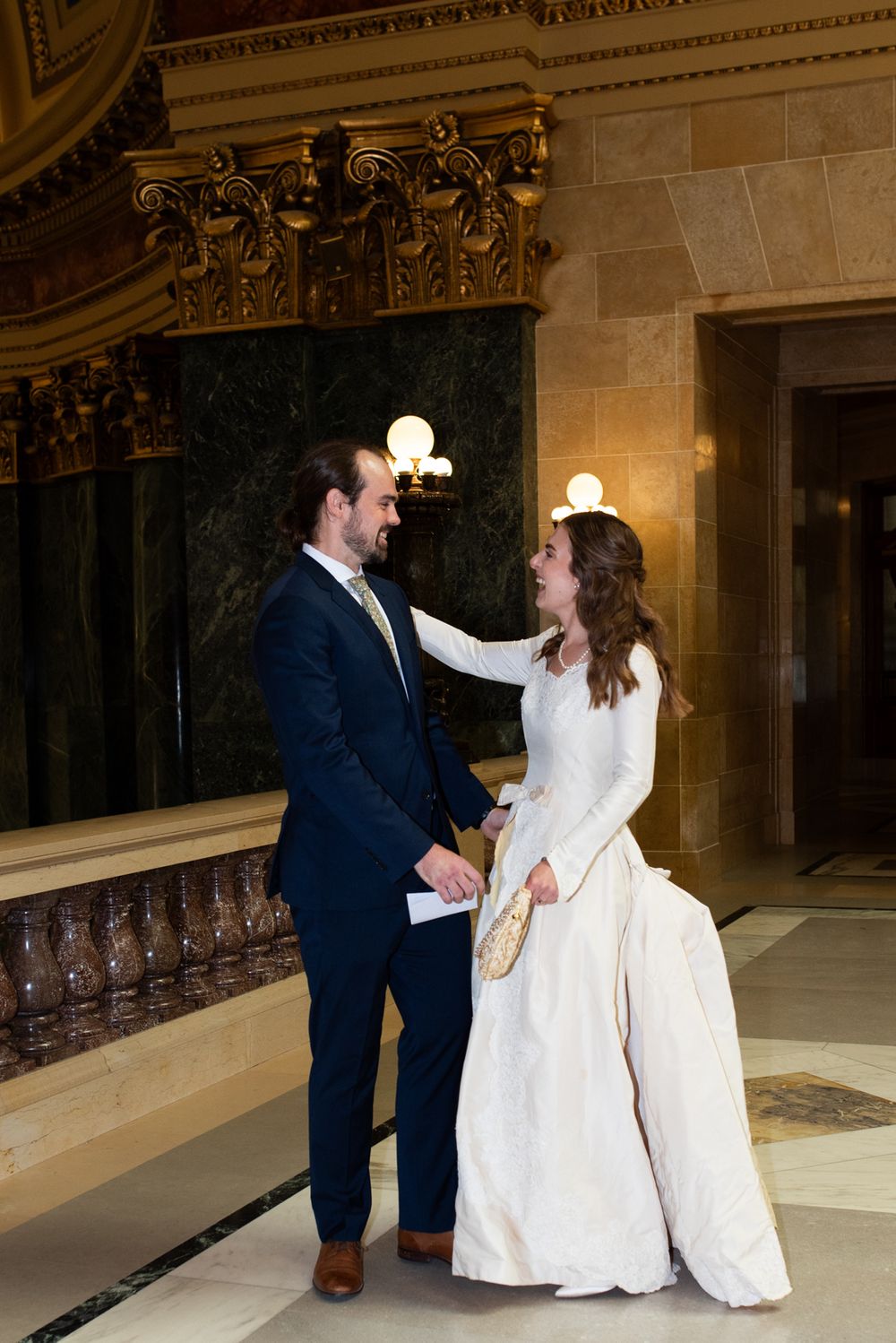 Bride and groom share a tender moment in an elegant marble building interior.