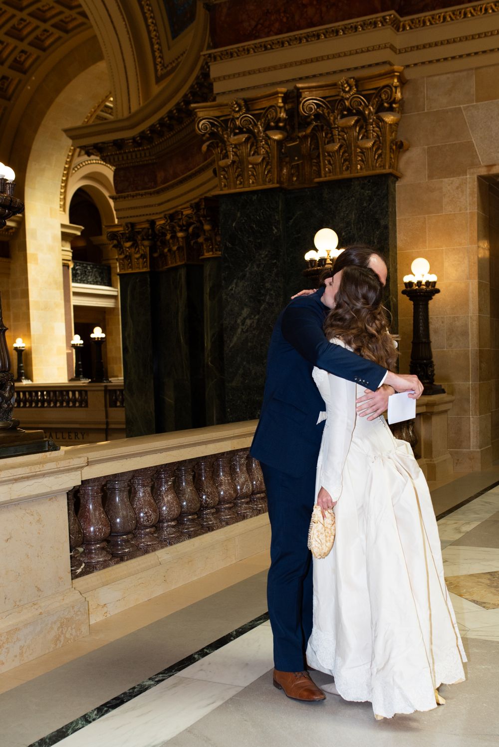 Bride and groom share a romantic embrace in an elegant ornate marble hall on their wedding day.