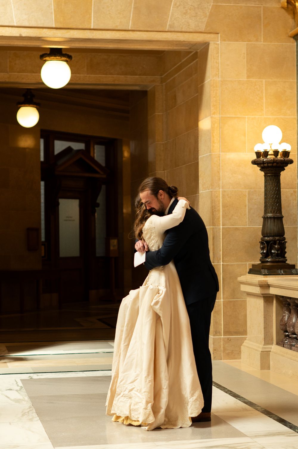 Couple shares a romantic embrace in a warmly lit ornate stone corridor.