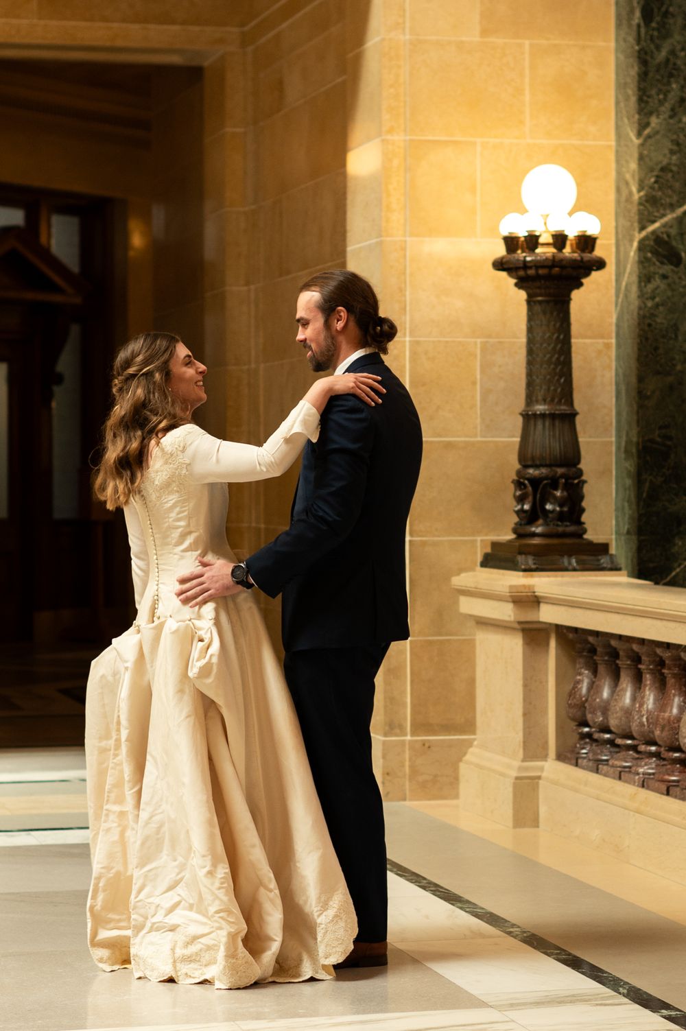 Bride and groom dance together in a grand historic building with ornate decor.