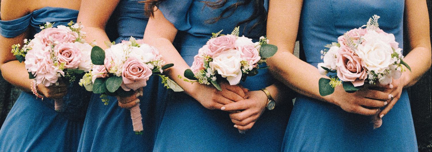 Bridesmaids in blue dresses holding pink and white rose bouquets with eucalyptus greenery at a wedding.