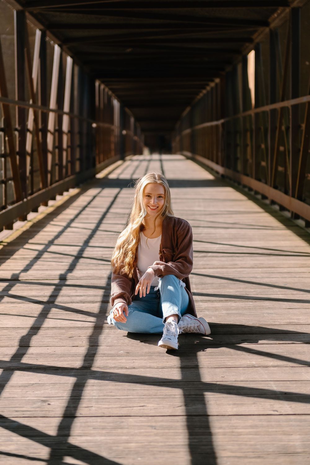 Beautiful natural lighting on wooden bridge creates shadows through railings as someone sits casually on the wooden planks.