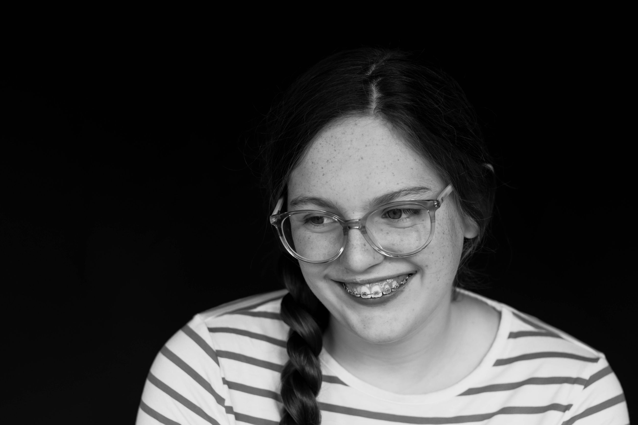 Black and white portrait of a smiling teen girl with braid, glasses, and braces.