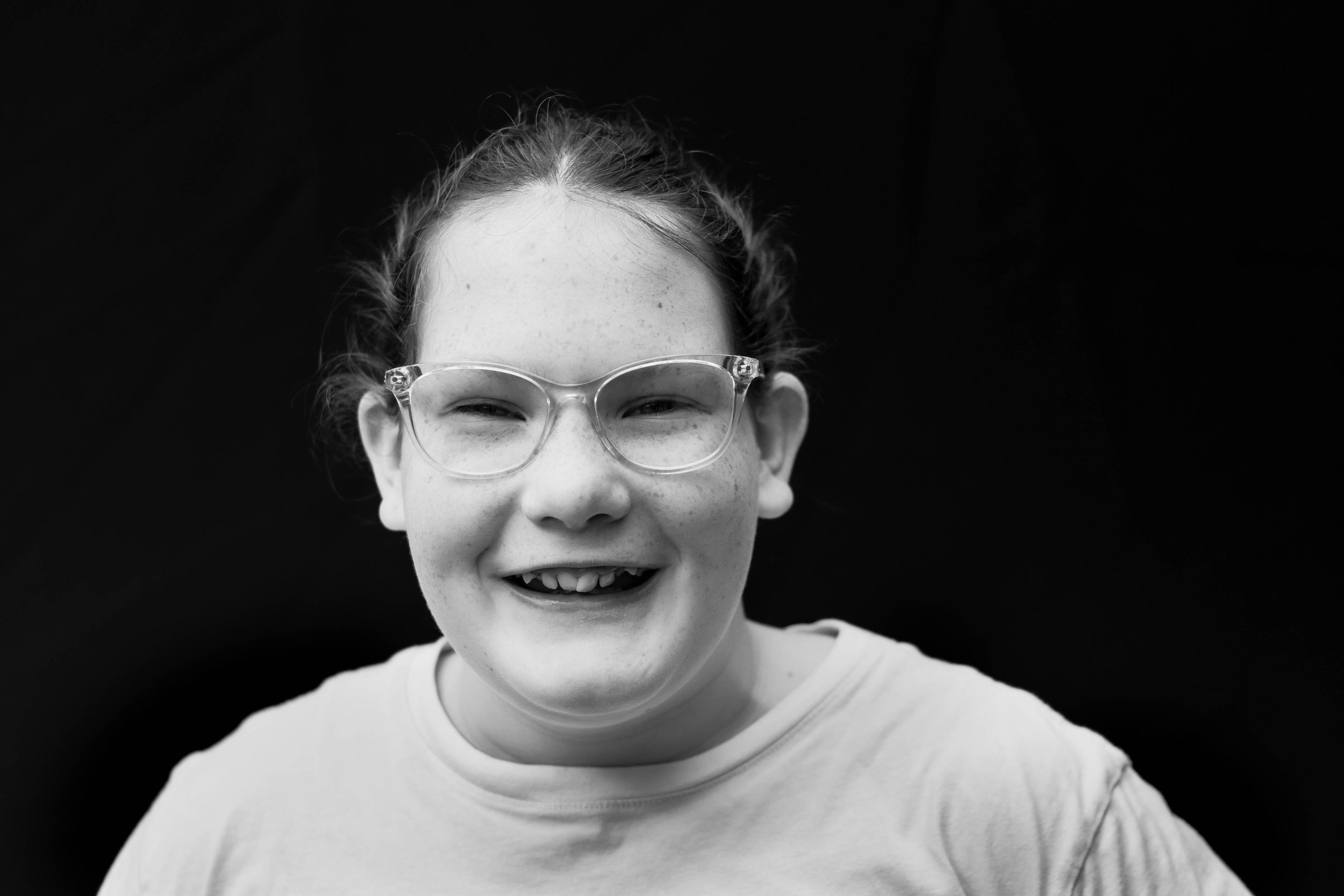 Black and white photo of a smiling young girl with glasses and hair pulled back.