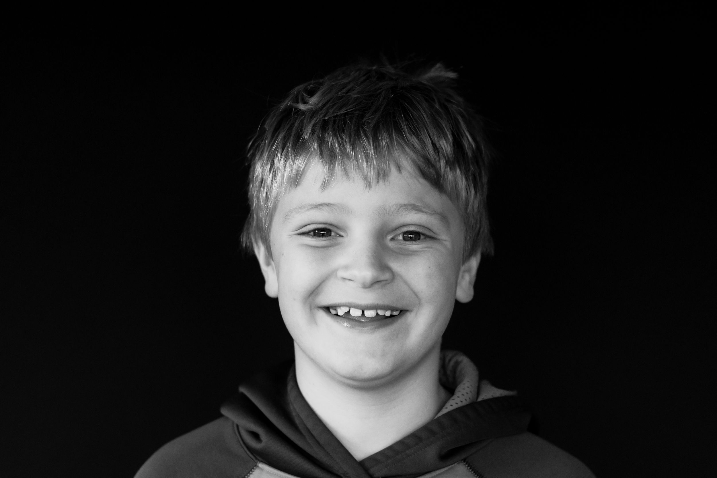 Black and white portrait of a happy young boy with a big smile and missing teeth.