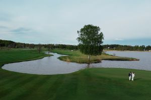 Aerial view of a scenic golf course with lush green fairways, sand bunkers, and a tranquil lake surrounded by trees.
