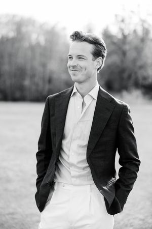 Black and white portrait of a smiling young man in a blazer and white shirt standing outdoors.