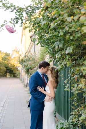 A romantic wedding couple embraces under green foliage on a sunlit path during their outdoor photo session.