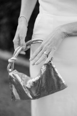 Black and white close-up of hands holding a beaded clutch purse showing elegant bridal accessories.