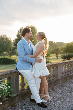 Romantic couple in light summer attire embracing on a stone terrace during golden hour.