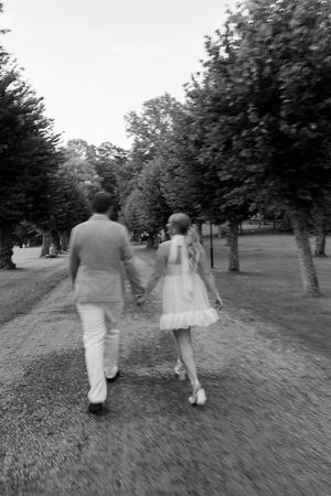 A romantic black and white photo of a couple walking hand in hand down a tree-lined path.
