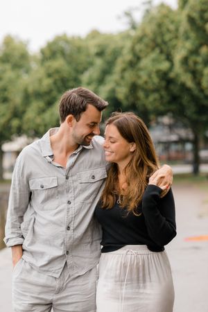 A couple shares an intimate moment outdoors, with him wearing gray and her in black and white clothing.