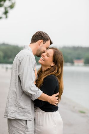 A romantic couple shares a tender moment while embracing on a lakeside shore.