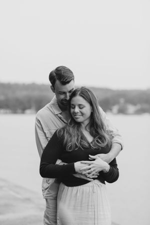 A romantic couple embraces by a lakeside in a heartfelt black and white portrait.