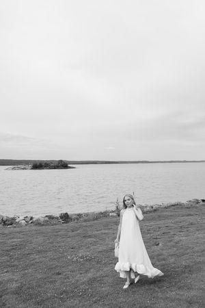 A child in a white dress twirls joyfully on a grassy coastal cliff overlooking a serene ocean view.