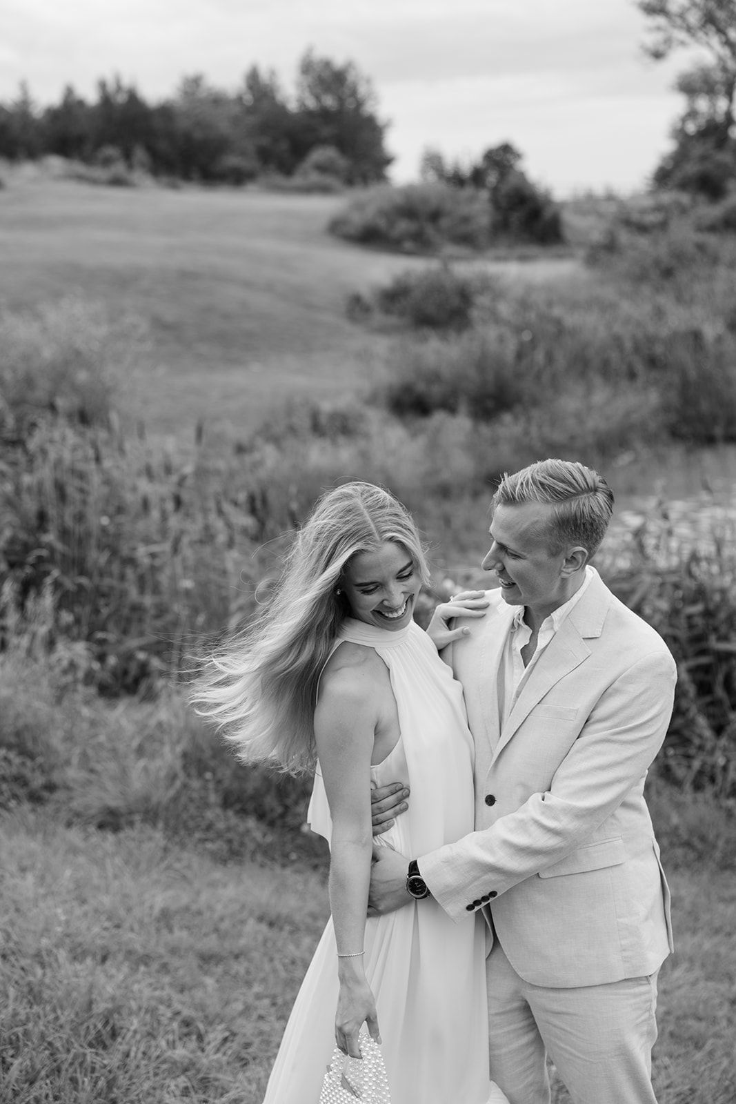A romantic black and white photo series showing a couple embracing in a meadow with flowing grass and natural scenery.