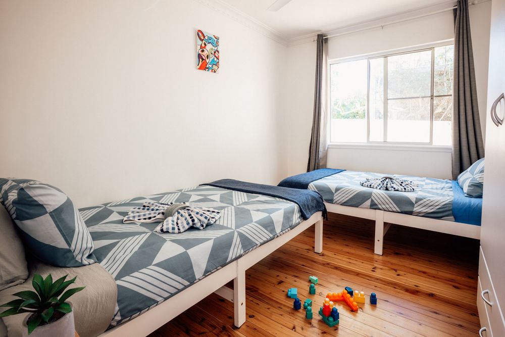 Twin bedroom with geometric blue bedding on white frames, hardwood floors, and natural light from a window.