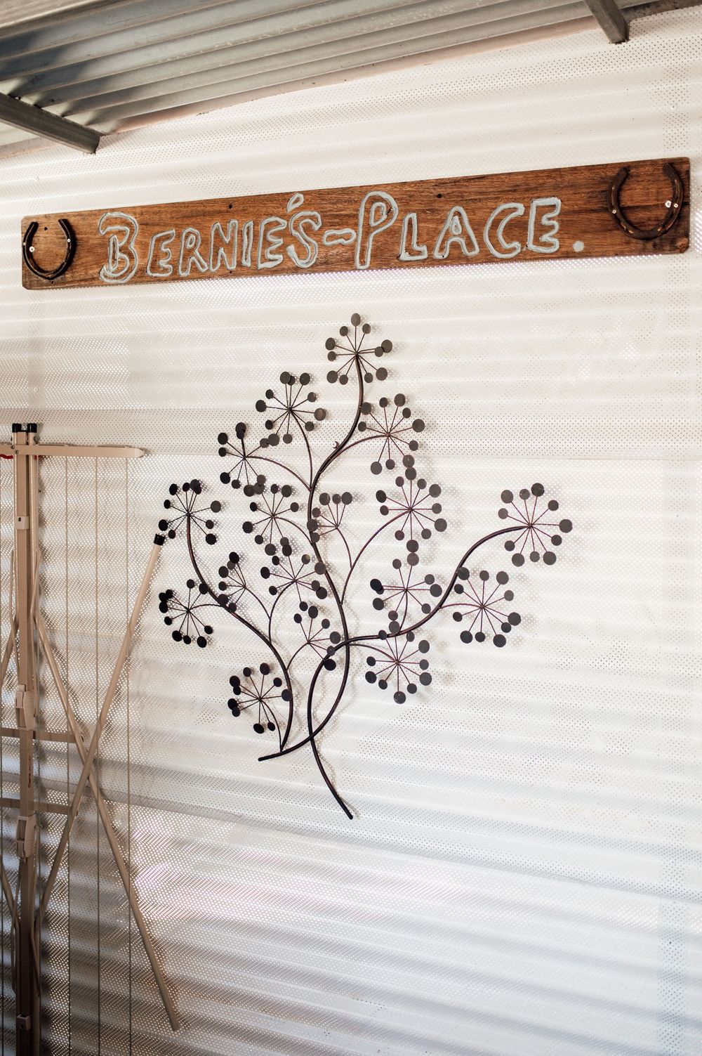 Bernie's Place rustic wooden sign with decorative metal botanical wall art on corrugated iron wall.
