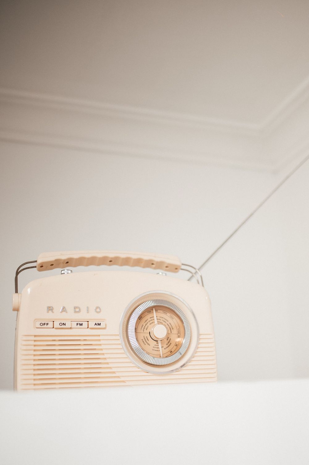 Vintage cream-colored retro radio with antenna on white shelf against white wall.