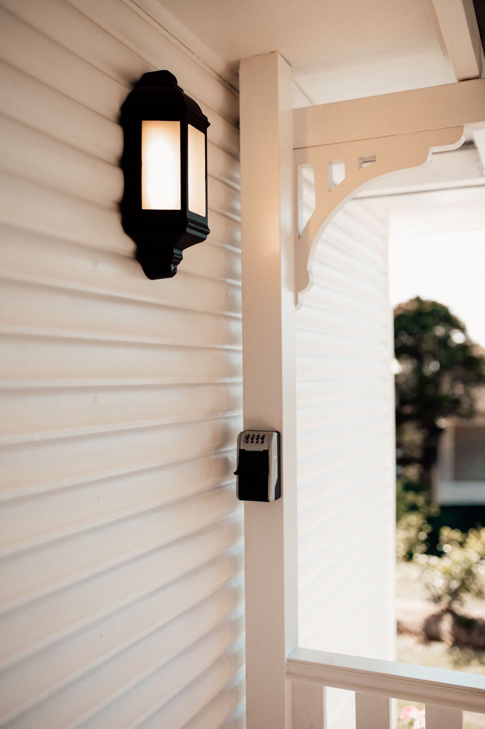Black lantern wall light on white weatherboard home exterior with decorative porch column and railing.