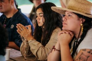 Young woman with long dark hair carefully examines natural fibers at an outdoor cultural craft workshop.