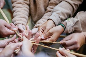 Multiple hands collaborate to weave and twist natural reed fibers together in a traditional craft.