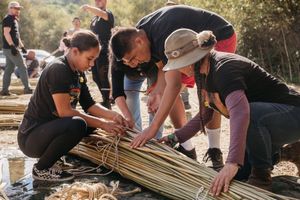 Group of people collaboratively weaving traditional reed mats together at an outdoor cultural workshop.