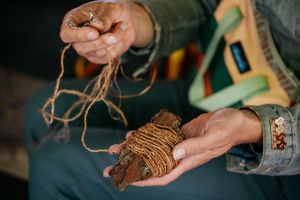 Close-up of hands holding a bundle of twine-wrapped wood and loose string for traditional crafting.