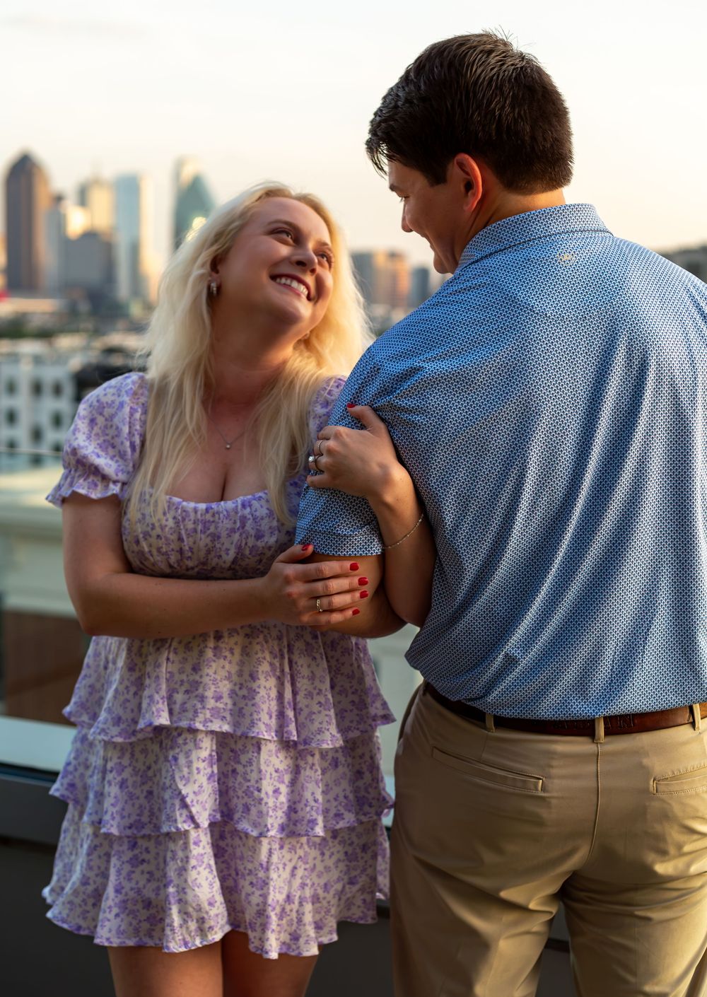 Happy couple embracing and laughing together on rooftop with city skyline at sunset.