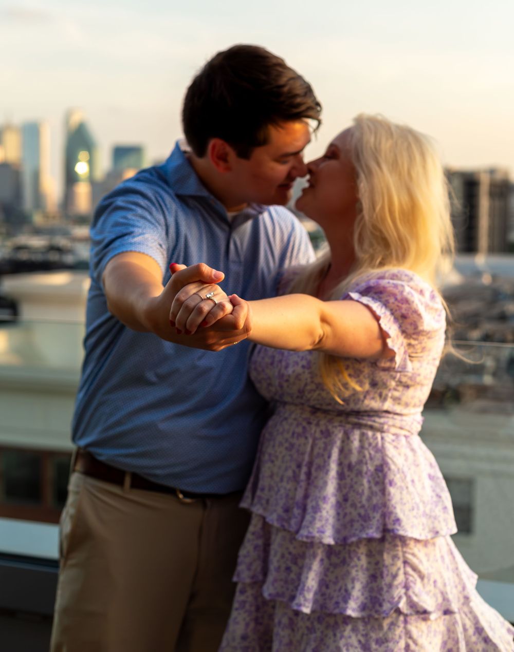 Couple sharing a romantic moment on a rooftop with a city skyline at sunset.