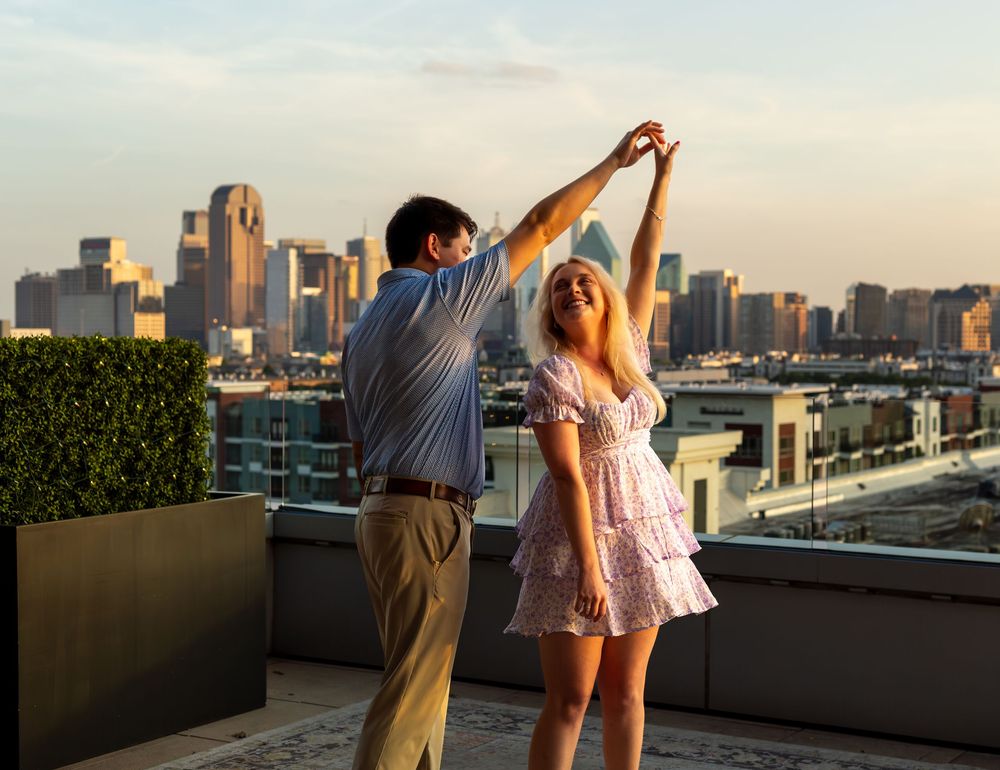 Couple dancing joyfully on rooftop terrace with stunning Dallas city skyline at golden hour.