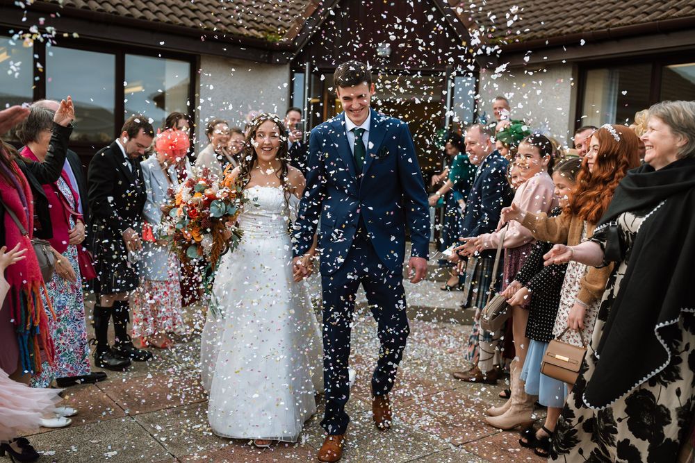 Wedding guests shower newlyweds with confetti during joyful outdoor celebration.